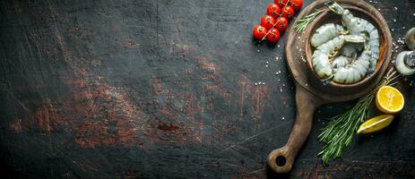 crudo gamberetti nel un' piatto su un' taglio tavola con ciliegia pomodori, rosmarino e tagliare Limone. foto