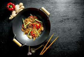 delizioso cellofan tagliatelle nel un' frittura padella wok con bacchette. foto