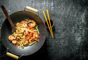 appena cucinato asiatico udon tagliatelle nel un' wok padella con soia salsa e bacchette. foto