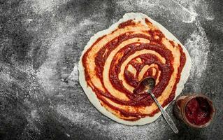 preparazione di Pizza. applicazione di pomodoro salsa su il lanciato Impasto. foto