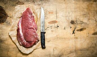 un' grande pezzo di crudo carne con un' macellaio coltello su il carta. foto