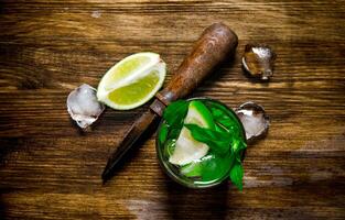 bicchiere di freddo cocktail , Ghiaccio, coltello e fette di lime su un' di legno tavolo. foto