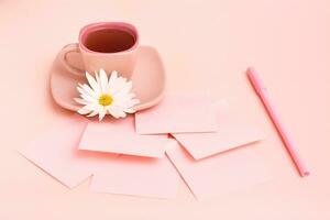 il concetto è rosa. rosa bevanda nel un' caffè tazza, lenzuola per scrivere, un' penna e un' crisantemo su un' rosa sfondo. foto