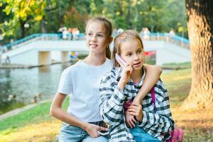 Due ragazze con premi il bottone telefoni rilassare nel un' estate parco foto