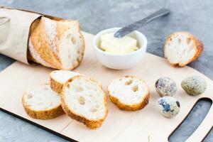 cucinando un' sostanzioso prima colazione con fresco baguette, burro e Quaglia uova su un' taglio tavola su un' tavolo foto