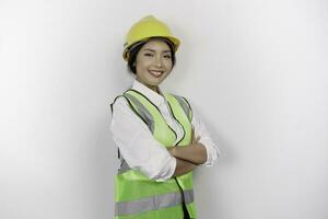 sorridente asiatico donna lavoro duro e faticoso lavoratore nel industria fabbrica, in posa con braccia piegato, indossare giallo sicurezza casco, verde veste e uniforme, isolato bianca sfondo. foto