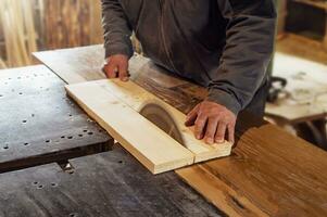 falegname seghe un' di legno tavola con un' carpenteria macchina. vecchio rustico carpenteria negozio. Lavorando su la lavorazione del legno macchina foto