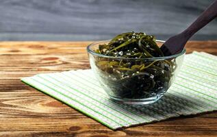 alga marina insalata. asiatico cucina. alga marina fuco nel un' bicchiere ciotola cosparso con sesamo semi, con un' di legno forchetta. laminari foto