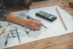 squadra di multietnico architetti Lavorando su costruzione piani nel incontro camera. ingegneri discutere su progetto nel ufficio. maturo uomo d'affari e donna in piedi in giro tavolo Lavorando su planimetria. foto