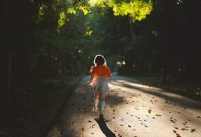 contento bambino asiatico ragazza sorridente. poco ragazza in esecuzione e sorridente a tramonto contento bambino ragazza sorridente. poco bambino in esecuzione a tramonto. carino bambino in esecuzione a terreno di gioco giardino. foto