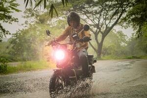 uomo equitazione piccolo enduro motociclo attraversamento superficiale torrente tra pioggia caduta a foresta foto