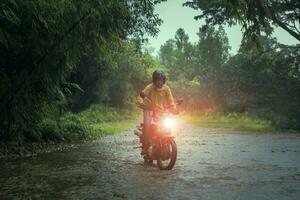 uomo equitazione piccolo enduro motociclo attraversamento superficiale torrente tra pioggia caduta a foresta foto