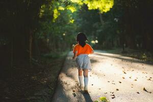 contento bambino asiatico ragazza sorridente. poco ragazza in esecuzione e sorridente a tramonto contento bambino ragazza sorridente. poco bambino in esecuzione a tramonto. carino bambino in esecuzione a terreno di gioco giardino. foto