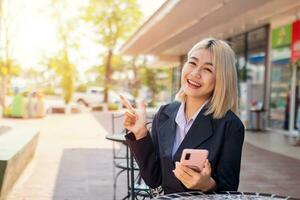 bellissimo attività commerciale contento giovane donna è consigliare un' confortevole posto per sedersi e freddo fare opera mentre Tenere Telefono. foto