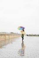 bella donna bruna con ombrello colorato che cammina sotto la pioggia foto