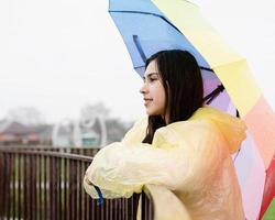 donna in piedi all'aperto con in mano un ombrello colorato, distogliendo lo sguardo foto