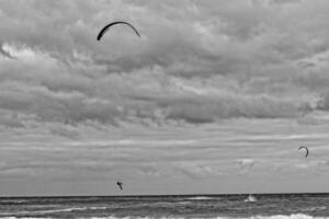 estate paesaggio con il oceano con buio nuvoloso onde e surfermi kit con paracadute galleggiante su il riva foto