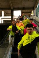 un' gruppo di asiatico uomini nel Limone verde giacche siamo in piedi con loro amici su il scala mobile foto