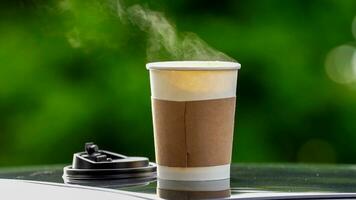 caffè porta via nel un' carta tazza su superiore di il auto tetto verde albero sfondo a Alba nel il mattina, selettivo messa a fuoco, morbido messa a fuoco. foto