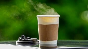 caffè porta via nel un' carta tazza su superiore di il auto tetto verde albero sfondo a Alba nel il mattina, selettivo messa a fuoco, morbido messa a fuoco. foto