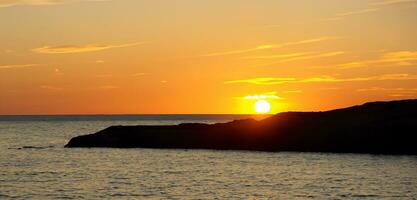 spiaggia mare sera a tramonto con rocce e colline arancia cielo foto