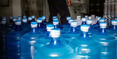 un' grande numero di plastica blu galloni di potabile acqua prodotti nel un' potabile acqua pianta quello siamo disposte nel un' riga in attesa per essere venduto. bevanda acqua fabbrica attività commerciale concetto foto