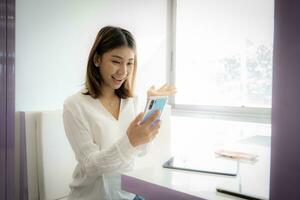bellissimo asiatico donna d'affari eccitato con un' testo Messaggio su sua Telefono dando sua un' indennità a opera. foto