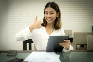 contento pollici su asiatico ufficio ragazza fare bene in linea i saldi su sua tavoletta per affari. foto