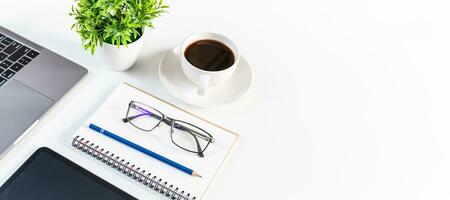 laptop, tazza di caffè, tablet e vaso sul tavolo bianco in un ufficio. ufficio di automazione concettuale utilizzando tecnologia, rete, internet. copia spazio a destra per un disegno, primo piano, vista pendenza sfondo bianco foto