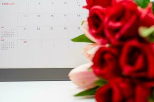 il calendario di febbraio con sfocato rosa fiore su il bianca scrivania, il concetto per san valentino giorno su 14 febbraio 2021 avvicinamento, e selettivo messa a fuoco foto