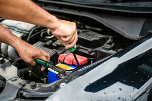 avvicinamento, il mani di un' maschio tecnico siamo utilizzando un' attrezzo per sostituire il auto batteria, parcheggiata a casa. nero macchina, il batteria è danneggiato. utensili avere pinze e cacciaviti. foto