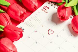 il marchio cuore su 14 calendario di febbraio con rosso tulipani fiore su il rosso sfondo su un' scrivania, il concetto per San Valentino giorno su 14 febbraio 2022. avvicinamento, selettivo messa a fuoco, sfocato sfondo foto