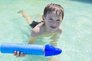 un' bambino nuotate nel il piscina con giocattoli. ragazzo bagna nel acqua foto