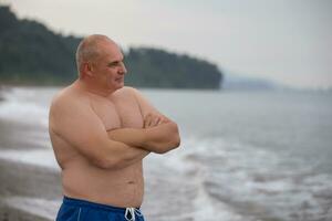 un anziano uomo di atletico costruire su il sfondo di il mare. foto