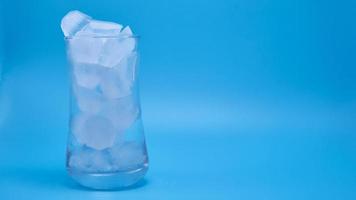 il ghiaccio in un bicchiere d'acqua che si scioglie su sfondo blu. foto