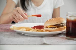 la donna che versa ketchup e mangia fast food. foto