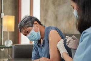 una dottoressa asiatica sta vaccinando un uomo anziano a casa. foto