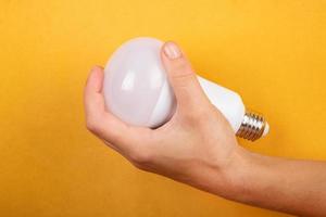 concetto di risparmio energetico, lampada a risparmio led in mano su sfondo giallo. foto