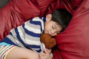 un' ragazzo è addormentato e abbracciare un' orsacchiotto orso su un' rosso materasso. foto
