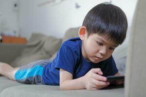 un' ragazzo felicemente bugie su il divano giocando con il suo Telefono. foto