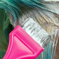 parrucchiere utilizzando rosa spazzola mentre l'applicazione dipingere per femmina cliente con Smeraldo capelli colore durante processi di candeggio capelli radici foto