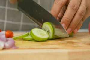 femmina mano utilizzando un' coltello per fetta cetrioli su un' taglio tavola. avvicinamento. donna con cucina coltello taglio cetriolo a casa. preparazione fatti in casa cibo foto