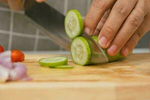 femmina mano utilizzando un' coltello per fetta cetrioli su un' taglio tavola. avvicinamento. donna con cucina coltello taglio cetriolo a casa. preparazione fatti in casa cibo foto