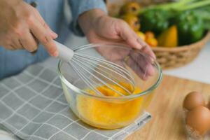 giovane donna cucinando nel luminosa cucina, mani sbattere uova nel un' ciotola posto su asciugamano e di legno tavolo. preparazione ingredienti per salutare cucinando. fatti in casa cibo foto