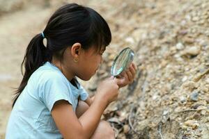 carino poco ragazza giocando con pietre e esplorando con un' ingrandimento bicchiere. poco ragazza studiando vario naturale materiali. alternativa formazione scolastica o istruzione a casa. foto