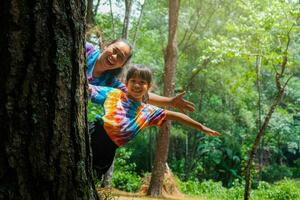 contento famiglia nascondiglio dietro a un' albero mentre giocando nel il parco. contento madre e figlia nascondiglio dietro a un' albero tronco. verde l'ambiente amichevole stile di vita. amore e proteggere natura concetto. foto