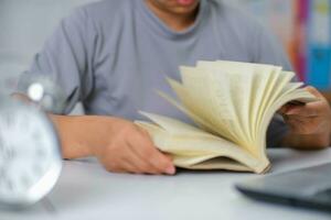 avvicinamento Immagine di asiatico donna seduta a un' tavolo lettura un' libro nel il vivente camera. foto