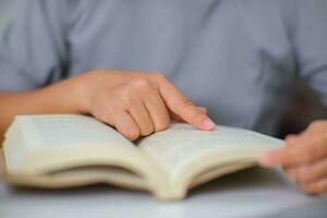 avvicinamento Immagine di asiatico donna seduta a un' tavolo lettura un' libro nel il vivente camera. foto