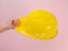 avvicinamento di femmina ingegnere mano Tenere giallo sicurezza casco su rosa sfondo. umano mano Tenere un' difficile cappello. foto