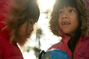 Due carino asiatico ragazze apprendimento un' modello di il mondo su natura sfondo e caldo luce del sole nel il parco. bambini imparare attraverso educativo giocare attività. terra giorno. mondo ambiente giorno. foto